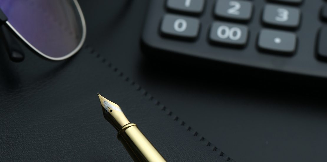golden pen,notebook,calculator and glasses on black desk